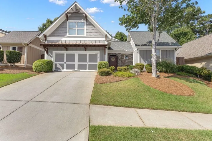 Gabled facade with horizontal siding, stone accents, decorative garage door, and established landscaping