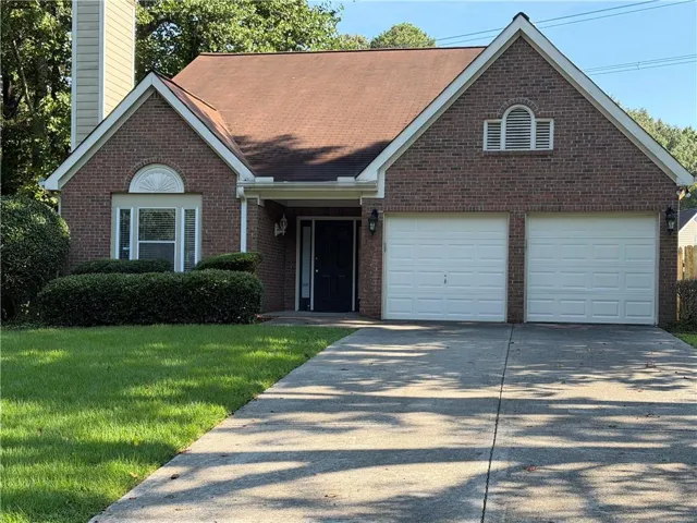Brick facade with a two-car garage, mature landscaping, and a concrete driveway