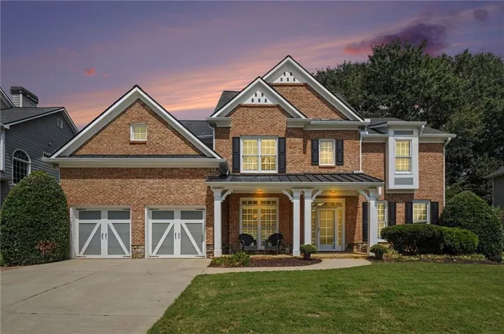 Brick facade with multiple gables, covered entry porch, two-car garage with decorative doors, and established landscaping