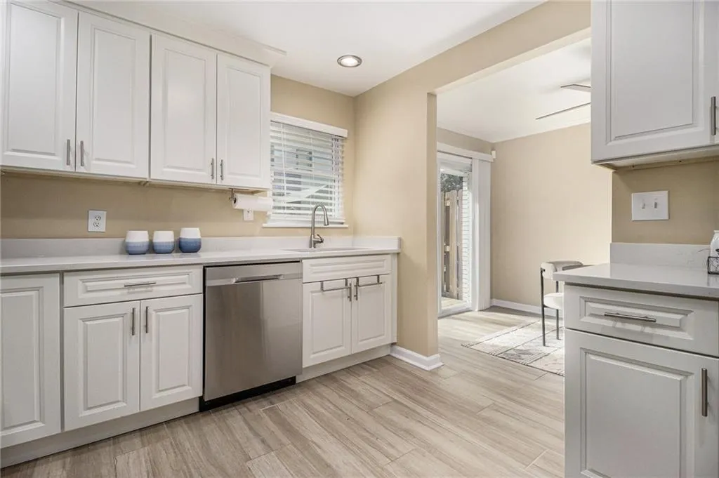Kitchen featuring stainless steel dishwasher, a sink, light countertops, white cabinetry, and ornamental molding