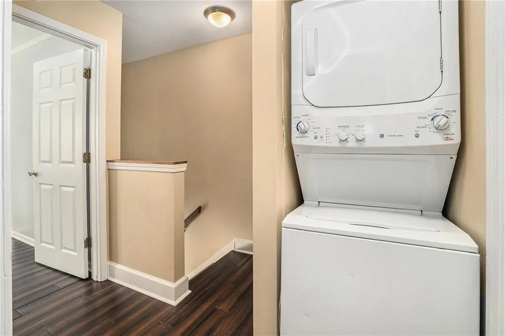Laundry room with stacked washer / drying machine, dark wood finished floors, and baseboards