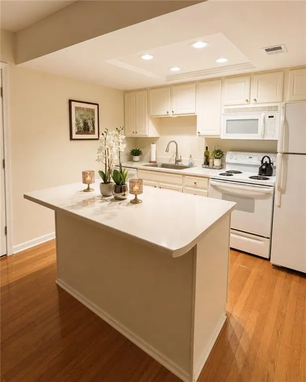 Kitchen featuring a central island with countertop, recessed lighting, wood-finish flooring, white cabinetry, and white appliances