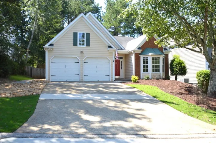 Two-car garage, bay window with copper-finish roof, brick and siding exterior, concrete driveway, and front lawn with mature trees