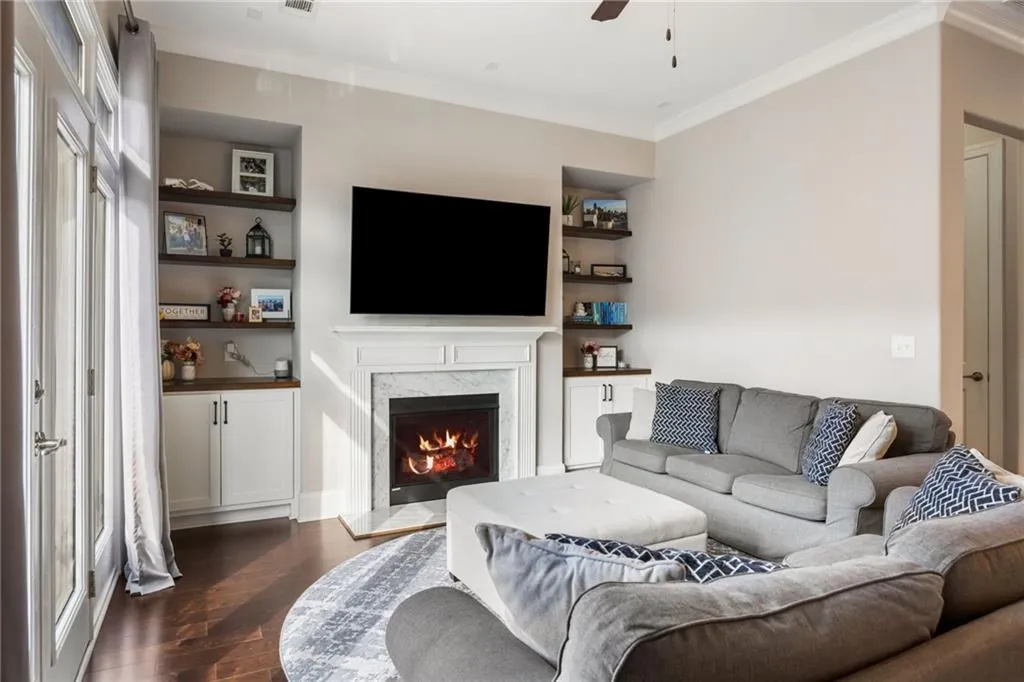 Living room featuring dark wood finished floors, ornamental molding, a high end fireplace, a ceiling fan, and built in shelves
