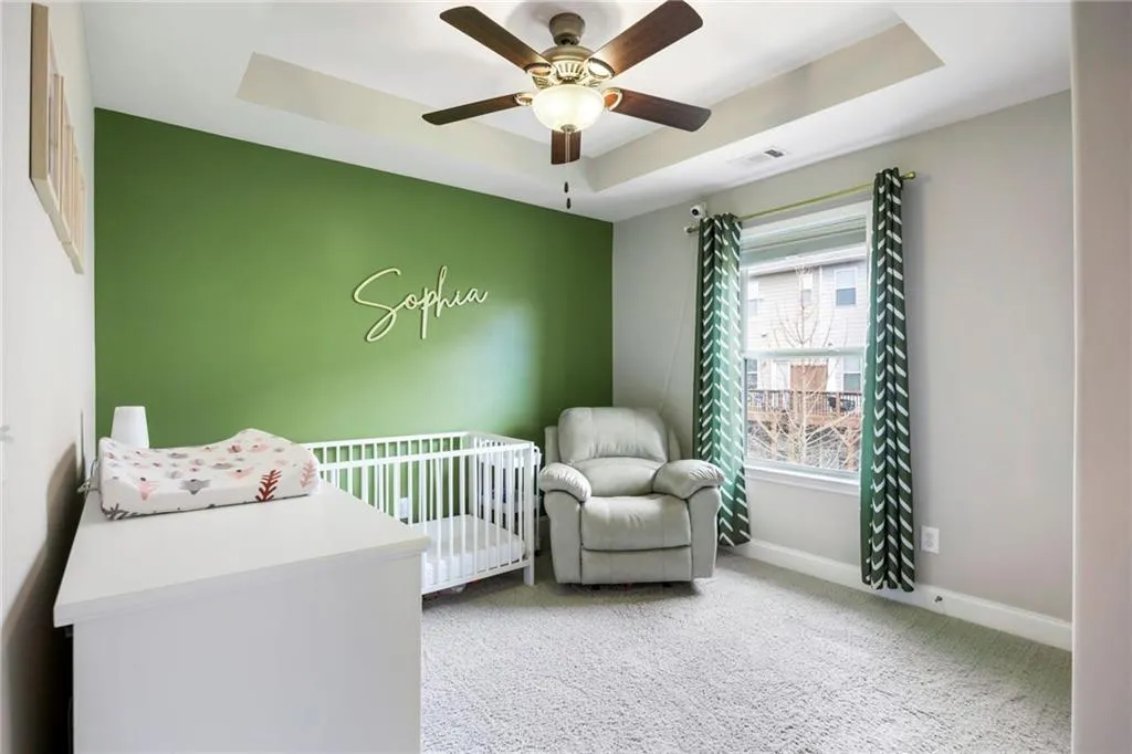 Bedroom featuring a tray ceiling, light carpet, a crib, and ceiling fan