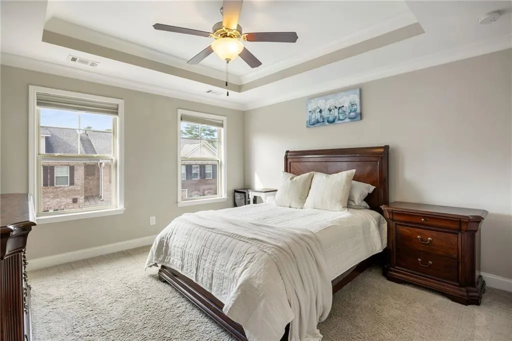 Bedroom with light carpet, a tray ceiling, ornamental molding, and a ceiling fan