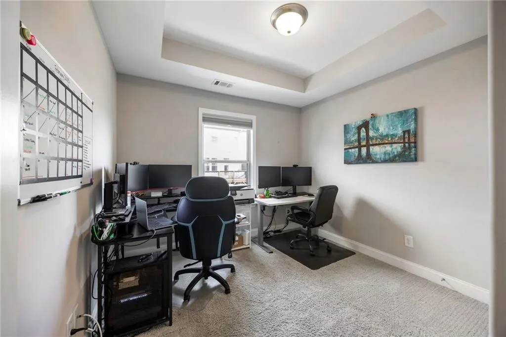 Home office featuring a raised ceiling and light colored carpet