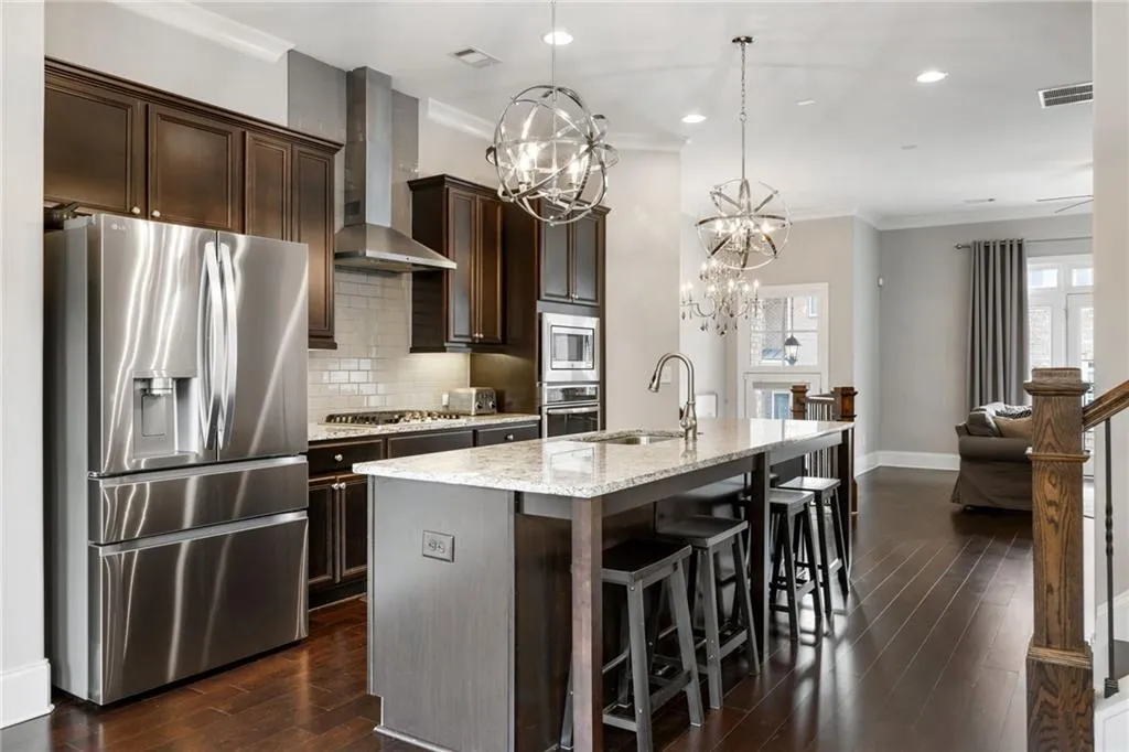 Kitchen featuring stainless steel appliances, tasteful backsplash, ornamental molding, wall chimney range hood, and light stone counters