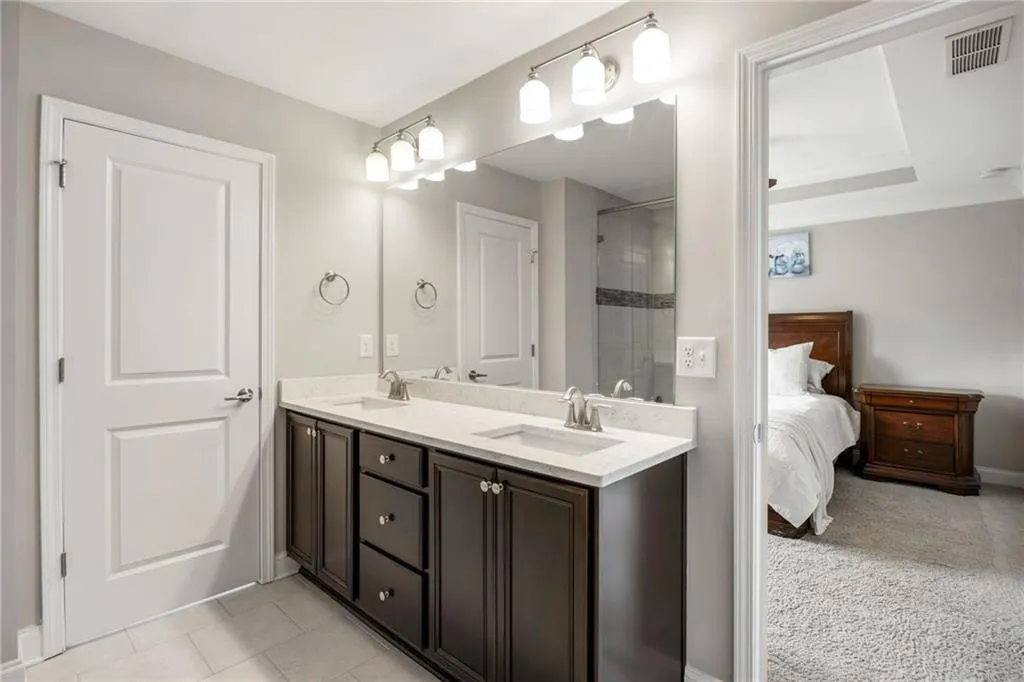 Ensuite bathroom featuring double vanity, light tile patterned flooring, tiled shower, and light carpet