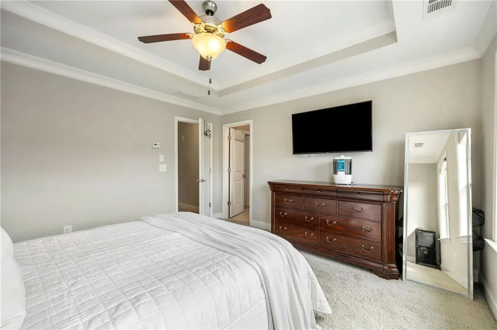 Bedroom with a raised ceiling, light carpet, a ceiling fan, and crown molding
