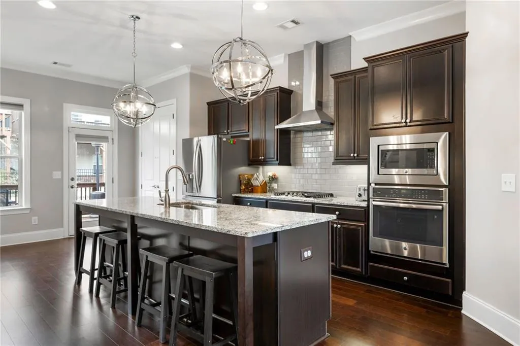 Kitchen with decorative backsplash, appliances with stainless steel finishes, dark brown cabinets, a kitchen breakfast bar, and light stone counters