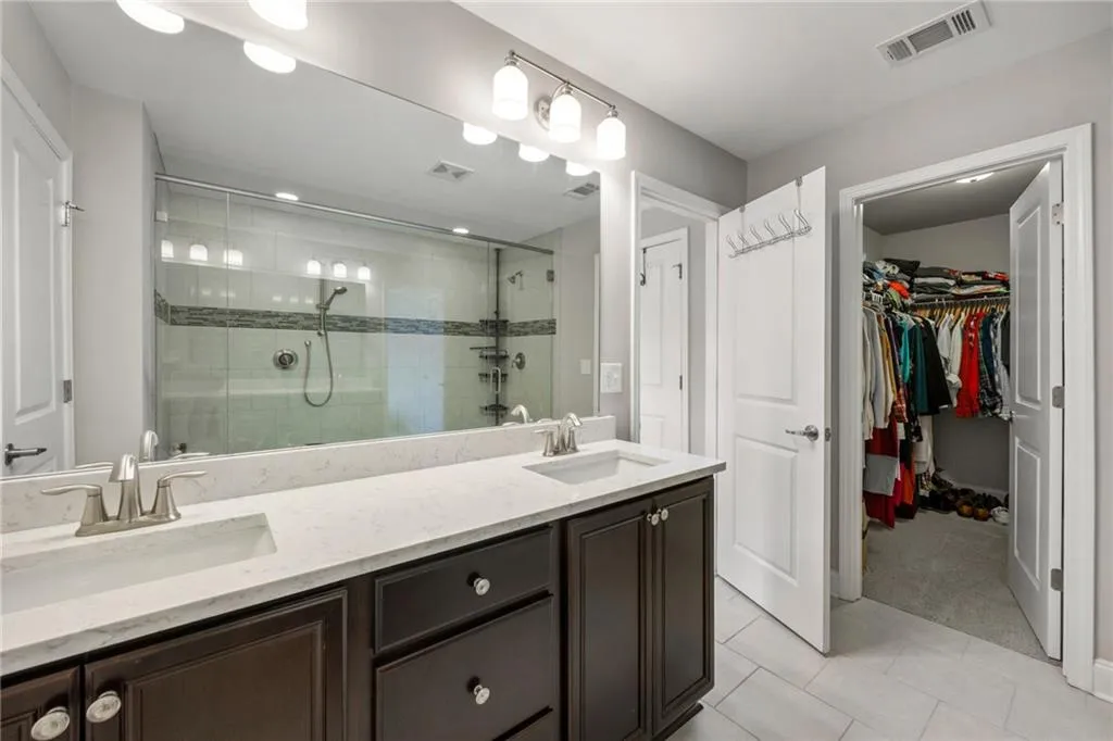 Bathroom featuring double vanity, light tile patterned floors, a walk in closet, a shower stall, and light colored carpet
