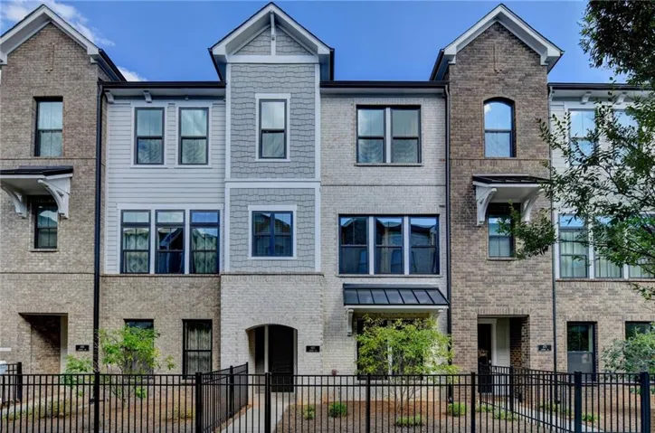Three-story townhouse with brick and siding exterior, black-framed windows, and wrought iron fencing