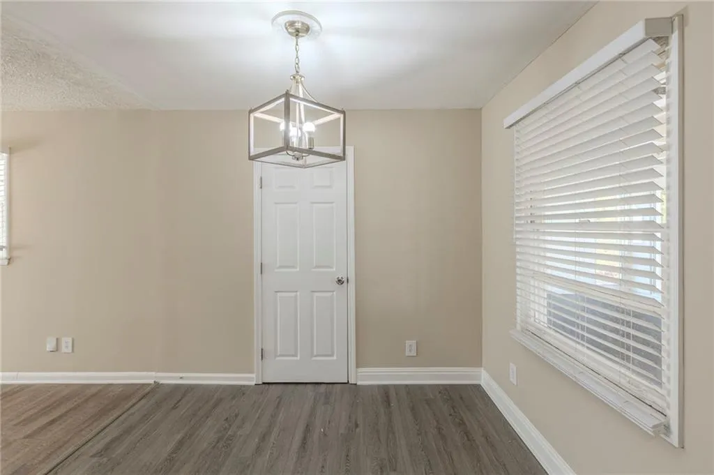 Unfurnished dining area with a notable chandelier, baseboards, and wood finished floors
