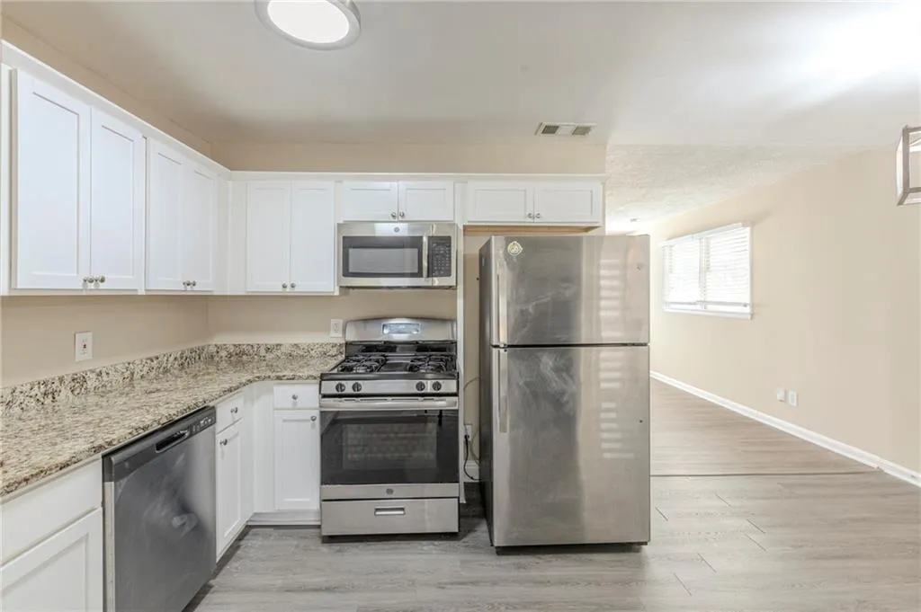 Kitchen featuring light wood finished floors, stainless steel appliances, visible vents, white cabinetry, and light stone countertops