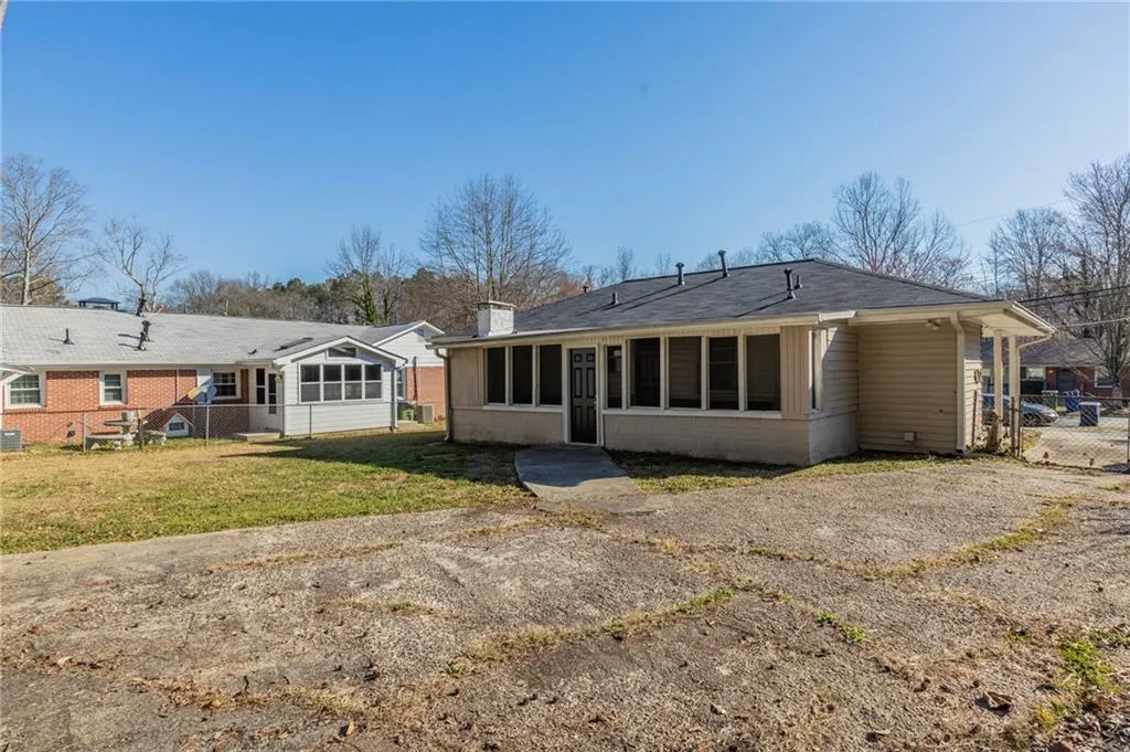 Back of house featuring concrete block siding, a chimney, a lawn, a sunroom, and fence