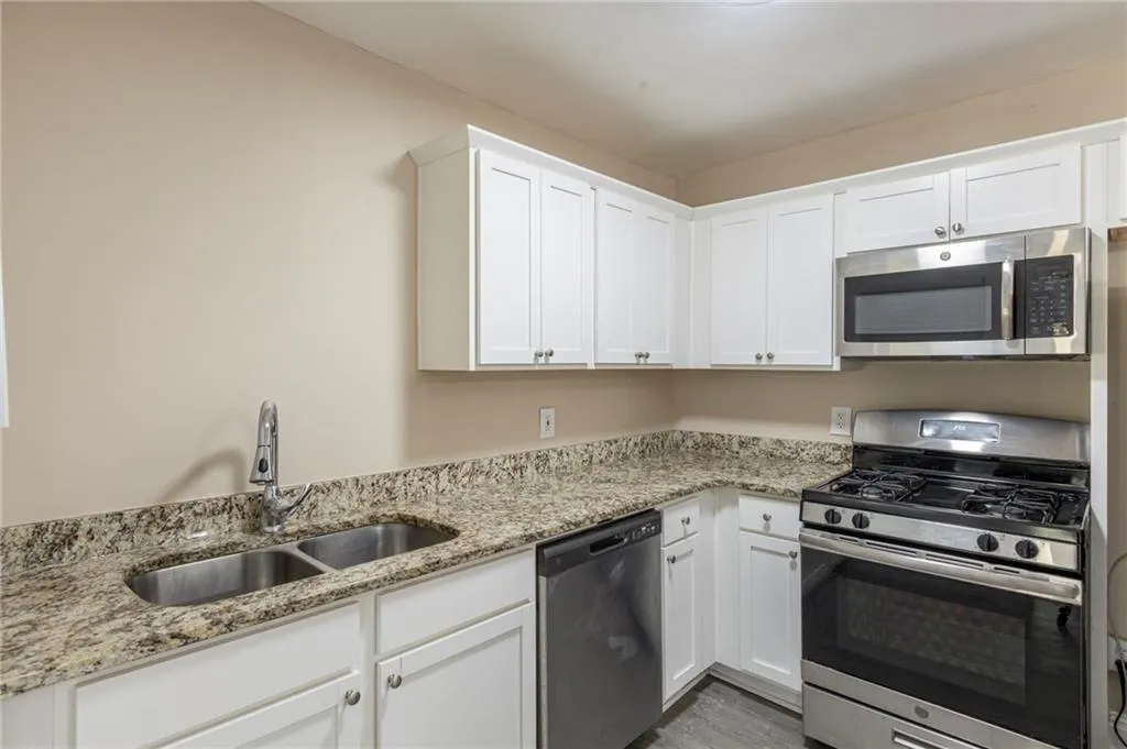 Kitchen featuring light stone countertops, appliances with stainless steel finishes, white cabinets, and a sink