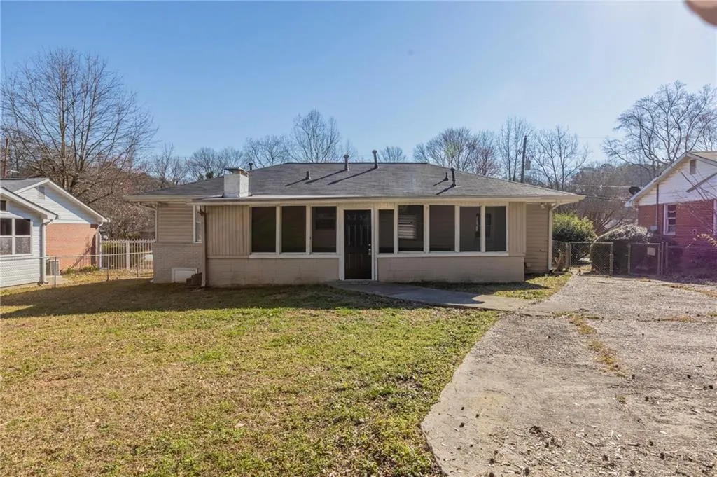 Rear view of property featuring a shingled roof, concrete block siding, a gate, fence, and a yard