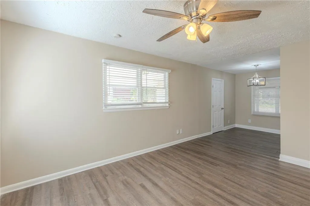 Unfurnished room featuring a textured ceiling, baseboards, wood finished floors, and ceiling fan with notable chandelier