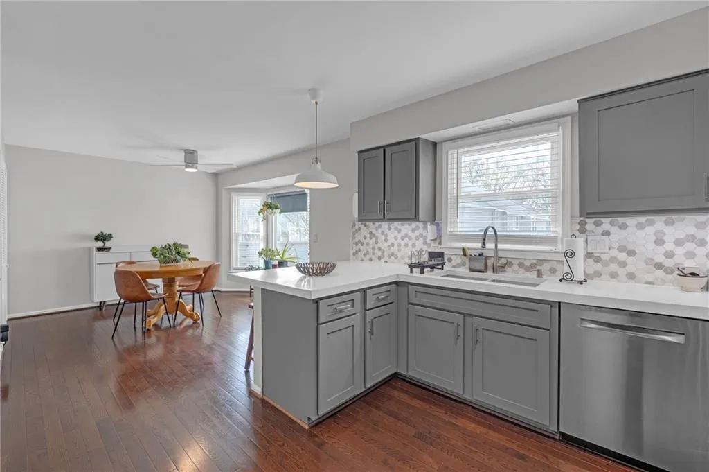 Kitchen with a peninsula, stainless steel dishwasher, gray cabinetry, pendant lighting, and dark wood-type flooring