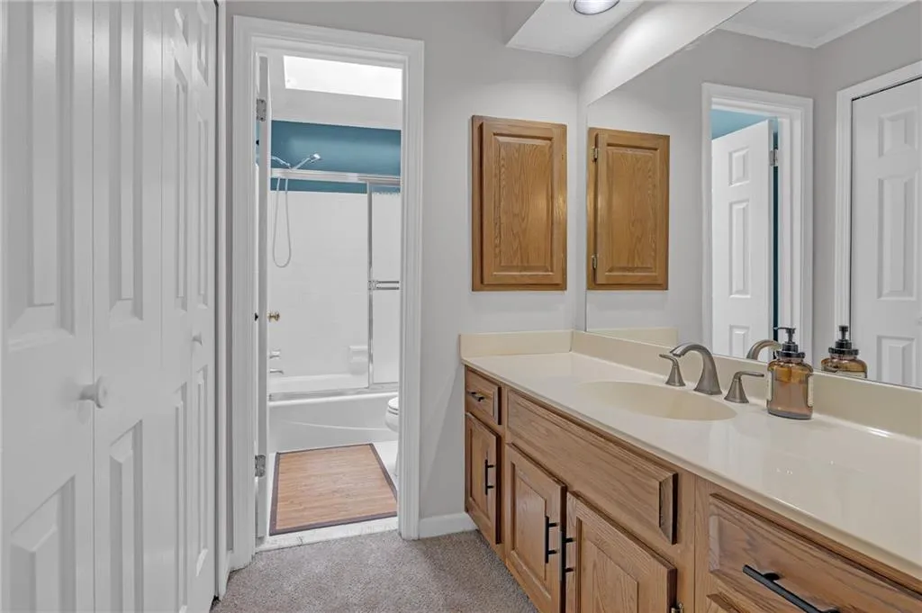 Bathroom with vanity, shower / bath combination with glass door, light colored carpet, and a closet
