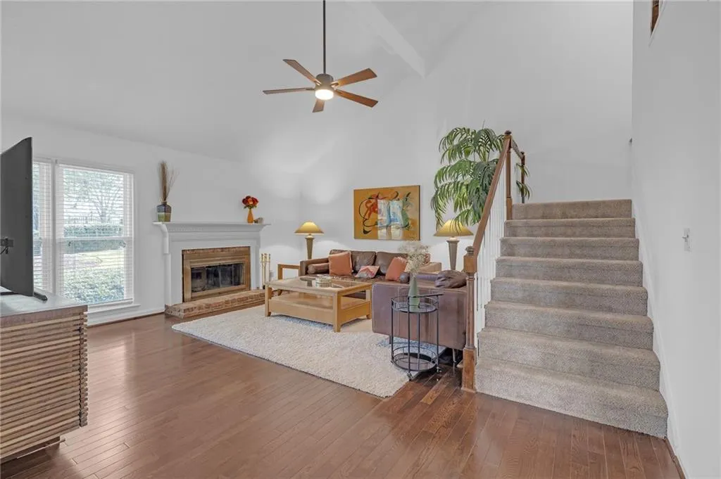 Living area with dark wood-style flooring, vaulted ceiling, ceiling fan, and a glass covered fireplace