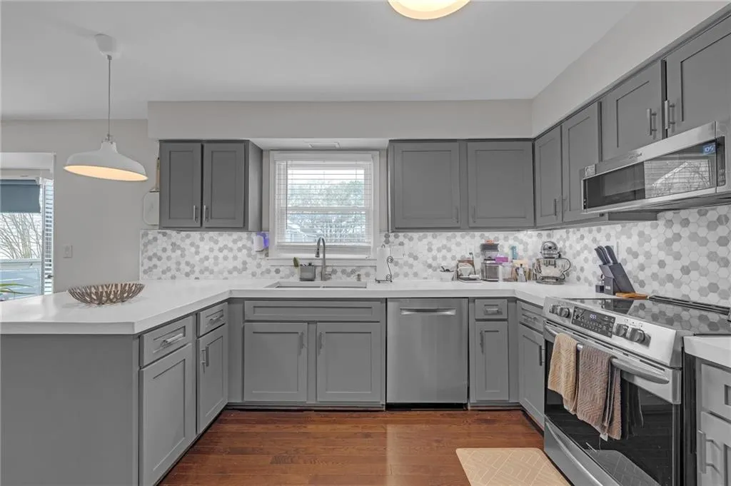 Kitchen with gray cabinets, a peninsula, stainless steel appliances, backsplash, and dark wood-style flooring