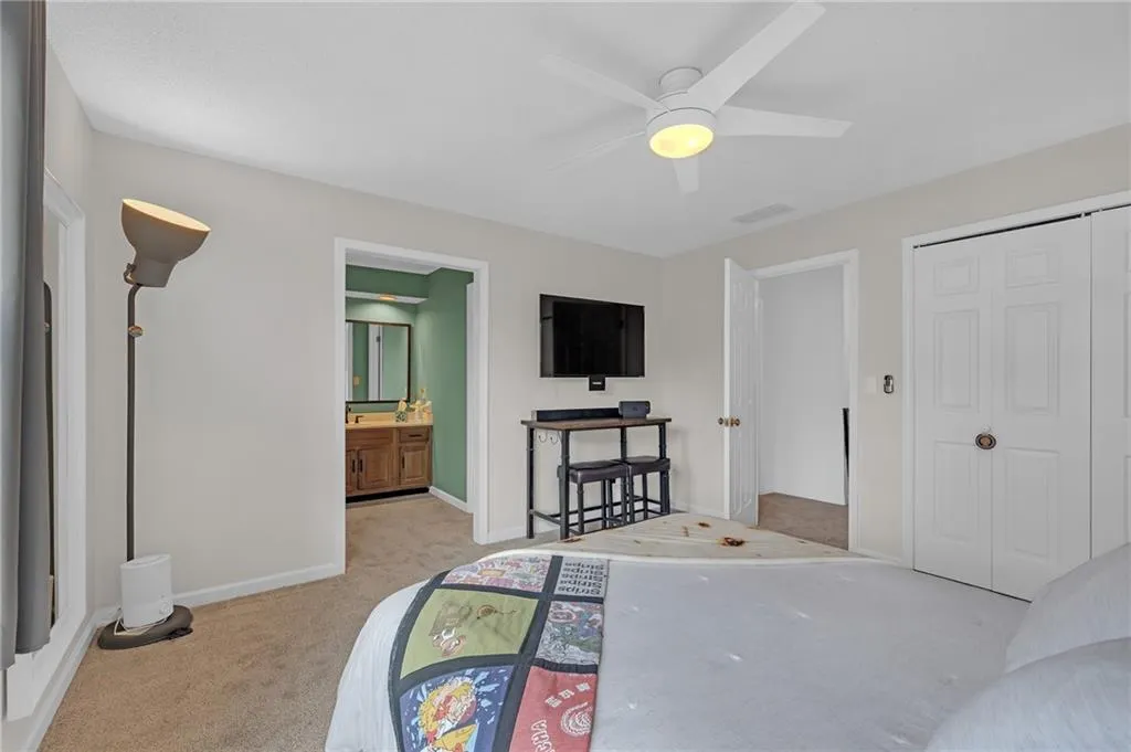 Bedroom with light colored carpet, a closet, ceiling fan, and ensuite bath