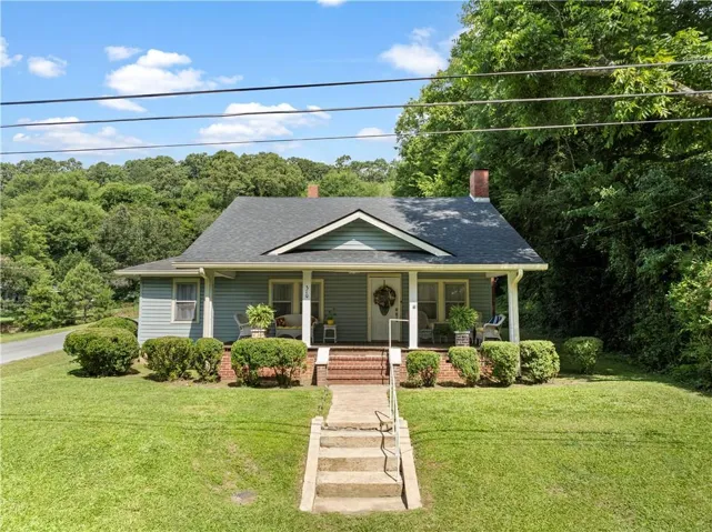 Light blue siding exterior featuring a covered front porch, brick foundation, and a dark shingle roof