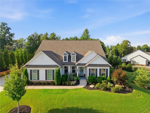 White exterior siding, dark roof, multiple gables, front walk, and manicured landscaping