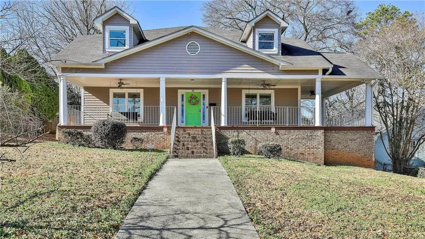 Craftsman-style exterior featuring a covered front porch, dormer windows, a vibrant green front door, brick foundation, and a concrete pathway leading to the entrance