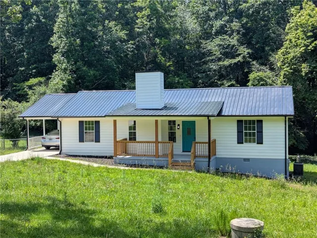 White siding exterior with a metal roof and a vibrant turquoise front door