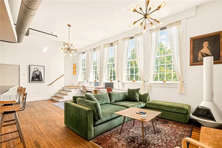 Spacious living area featuring high ceilings, wood-finish flooring, and multiple tall windows providing abundant natural light