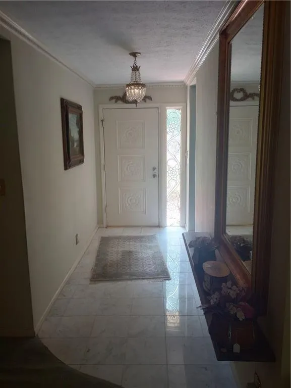 Foyer with ornamental molding, a textured ceiling, and a chandelier