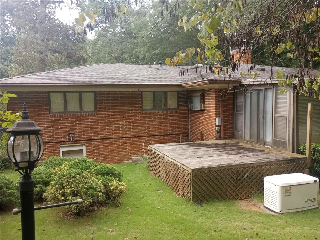 Rear view of house featuring a wooden deck, brick siding, a yard, and roof with shingles
