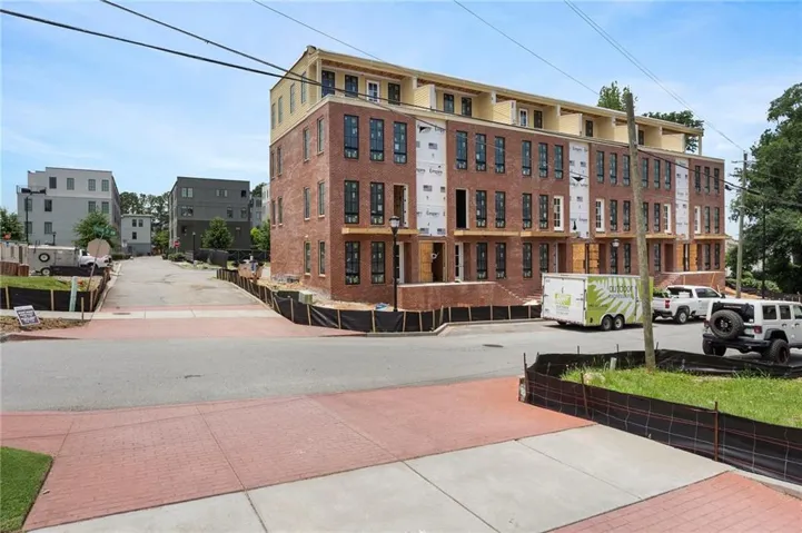 Four-story brick-front townhome structure featuring multiple window openings, a partial upper-level cladding, and individual entry points