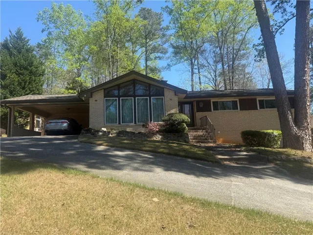 View of front of home featuring brick siding, a carport, driveway, and a front lawn