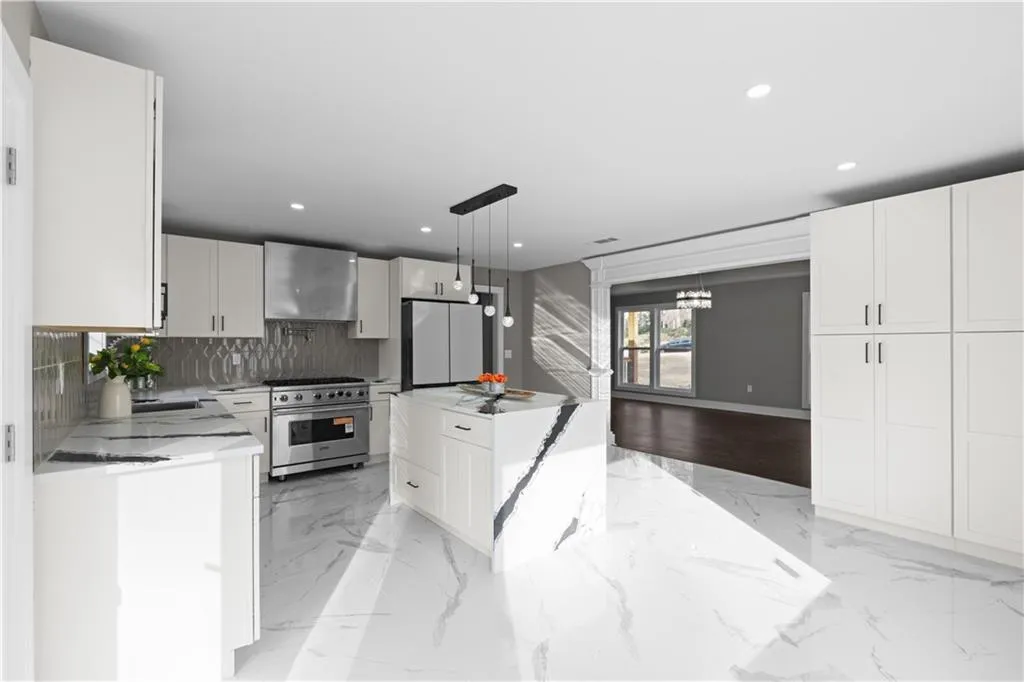 Kitchen featuring light marble finish floors, stainless steel stove, decorative light fixtures, a center island, and wall chimney range hood