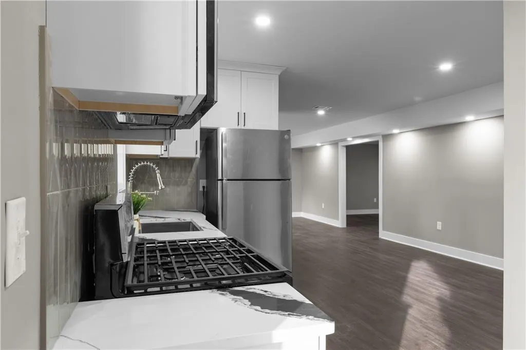 Kitchen featuring white cabinetry, under cabinet range hood, freestanding refrigerator, backsplash, and dark wood-style flooring