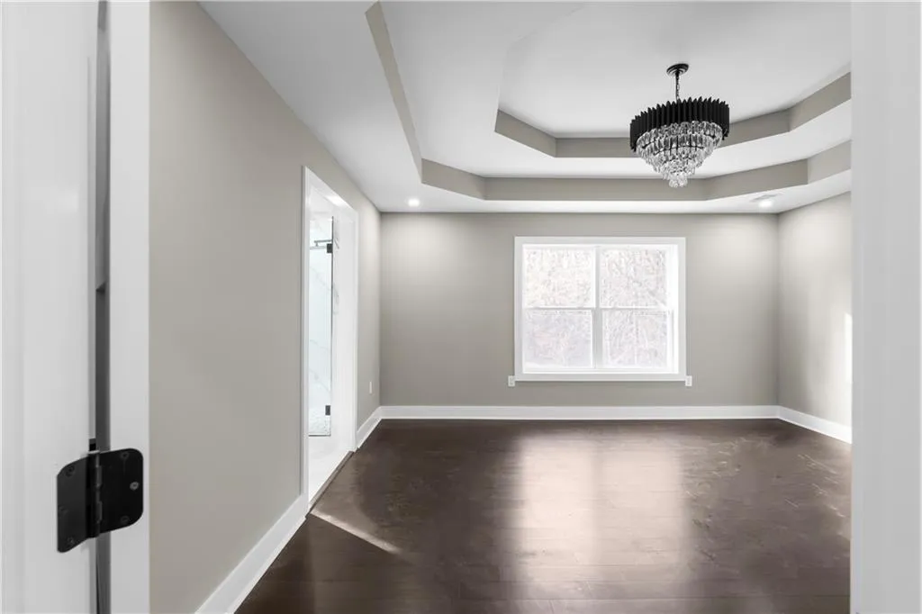 Spare room featuring dark wood finished floors, a chandelier, a tray ceiling, and recessed lighting