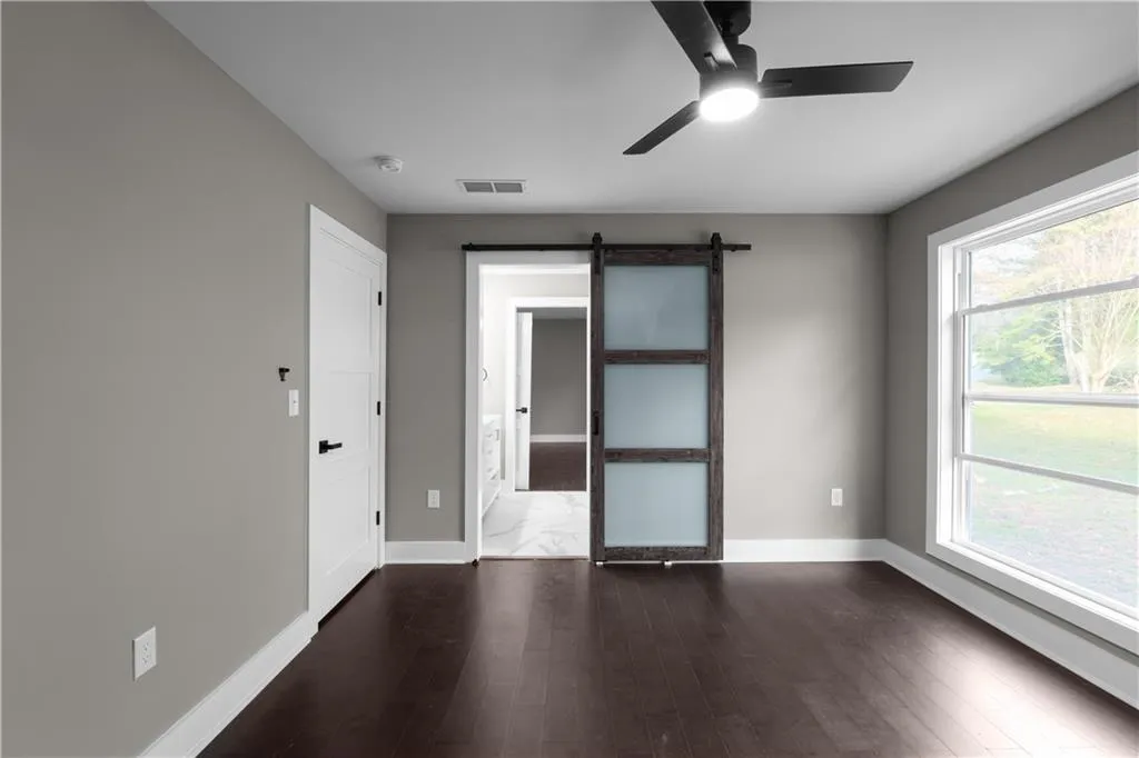 Unfurnished room featuring a barn door, dark wood-type flooring, and ceiling fan