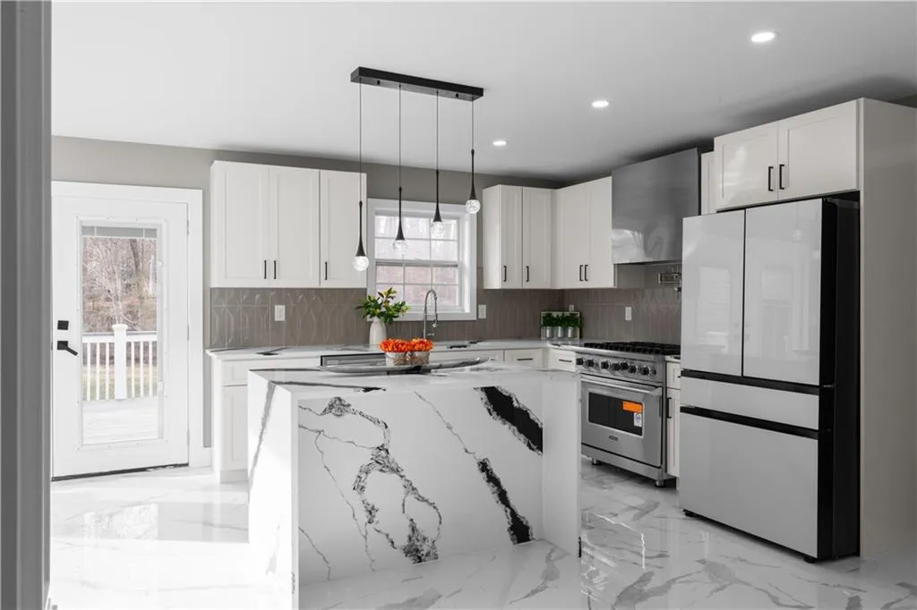 Kitchen featuring freestanding refrigerator, white cabinetry, hanging light fixtures, light marble finish floors, and recessed lighting