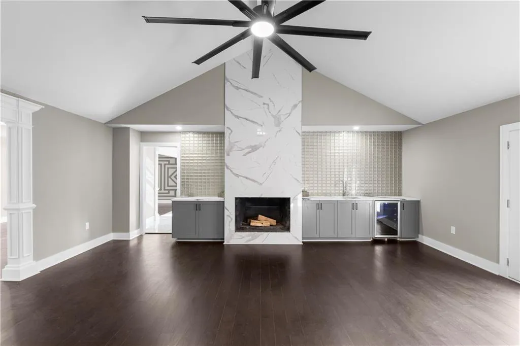 Unfurnished living room with dark wood-style floors, a fireplace, wine cooler, a ceiling fan, and high vaulted ceiling