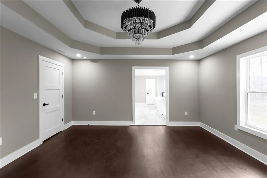 Empty room with dark wood-style flooring, a chandelier, a raised ceiling, and recessed lighting