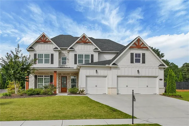 Two-story residence featuring a dark shingle roof, stone and siding exterior, multiple gables with exposed timber accents, a covered front entry with a wood-panel door, and a two-car garage with white doors