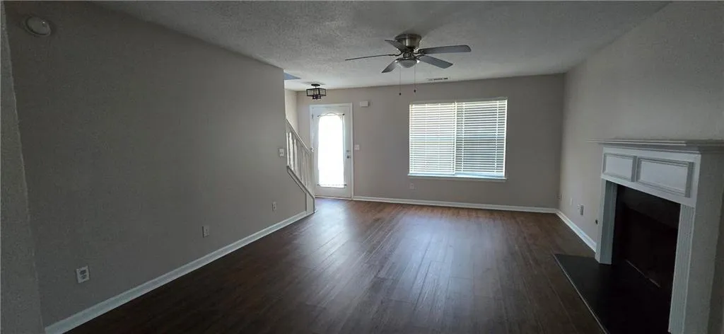 Spacious living area featuring rich wood-finish flooring, ceiling fan, and abundant natural light from dual windows