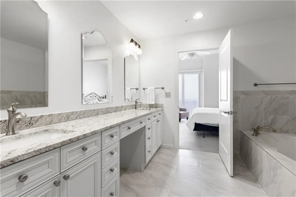Ensuite bathroom featuring double vanity, a bath, and light marble finish flooring