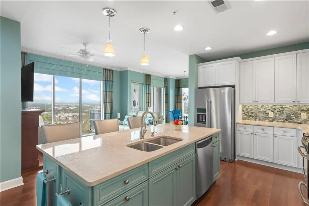 Kitchen featuring light stone countertops, hanging light fixtures, dark wood finished floors, stainless steel appliances, and a center island with sink