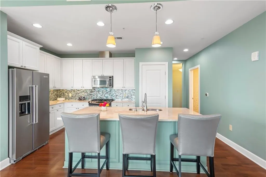 Two tone kitchen with stainless steel appliances, pendant lighting, a kitchen island with sink, light stone countertops, and a kitchen bar