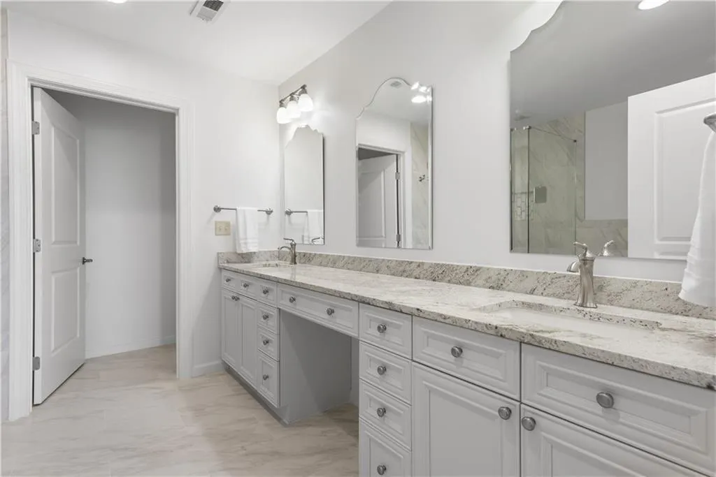 Full bath featuring double vanity, light marble finish floors, and a marble finish shower